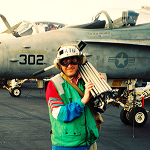 Sadler carrying tripod to report from the flight deck of the aircraft carrier USS America in the Mediterranean